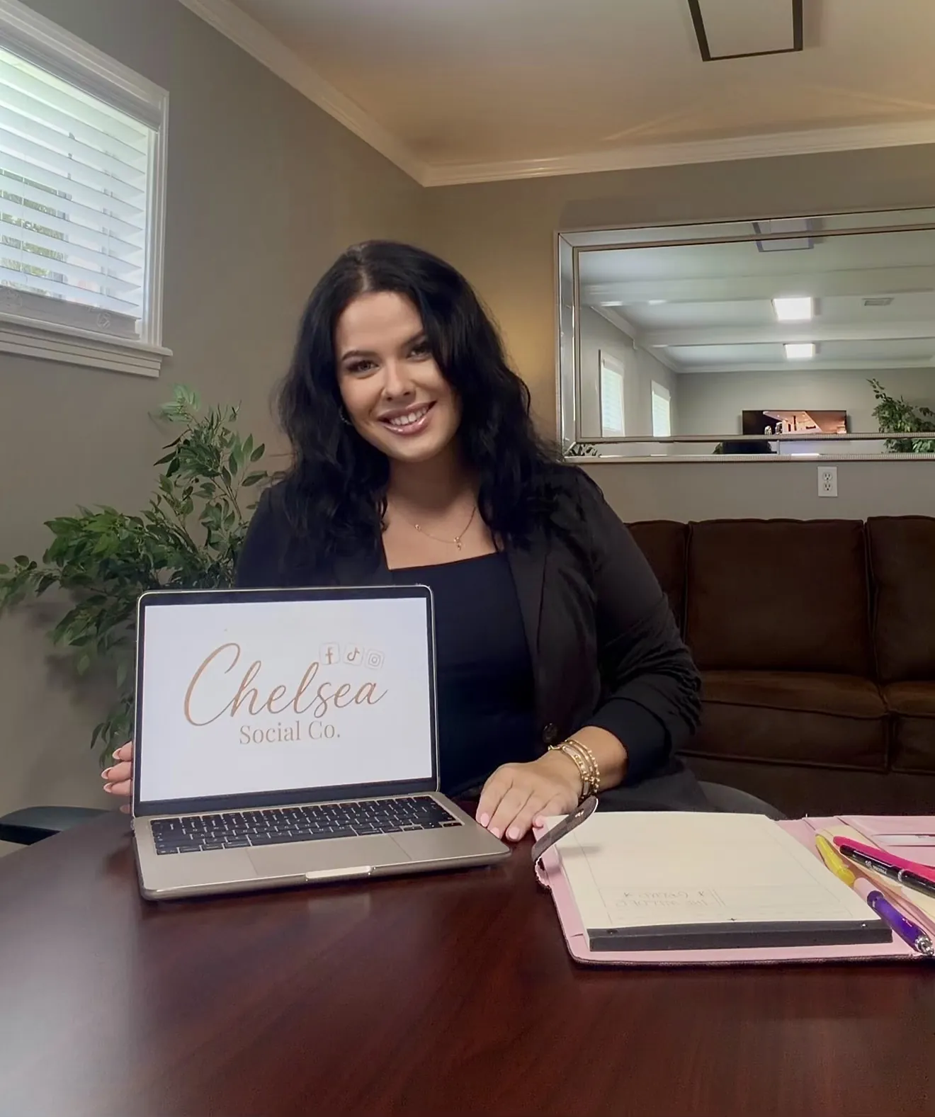 Chelsea smiling and holding a laptop showing the Chelsea Social Co. logo